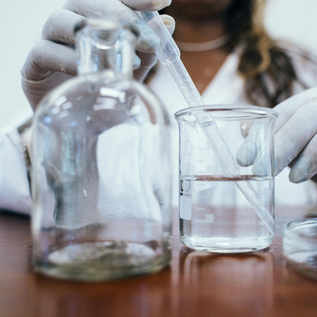 Person in a lab setting with gloves holding a beaker and pipette, with a blurred background.