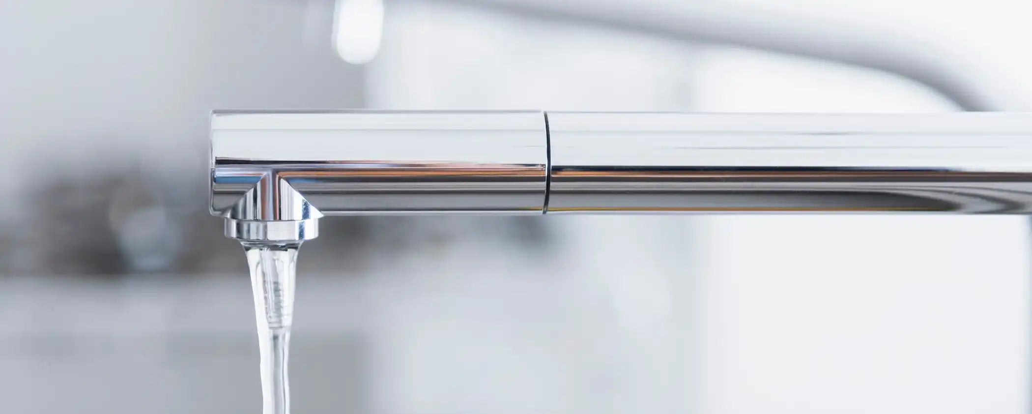 Close-up of a silver faucet with water flowing in a blurred kitchen background