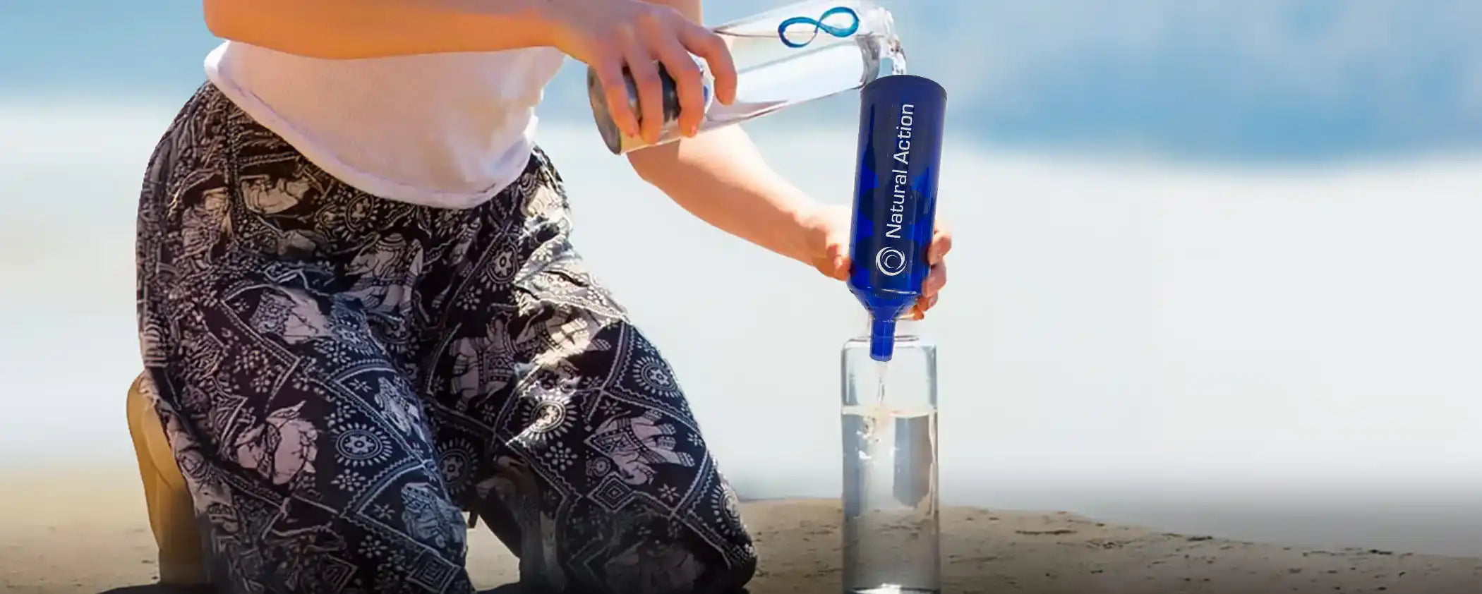 Person pouring water through a blue Natural Action Portable Unit into a glass on a beach.