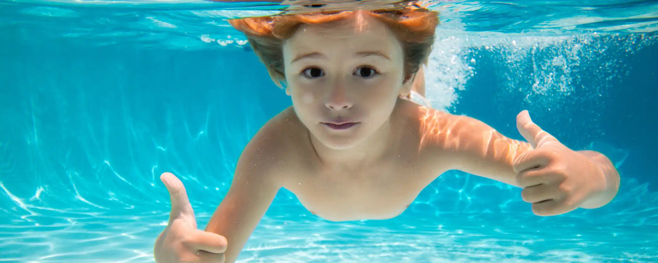Child underwater in a pool giving a thumbs-up gesture