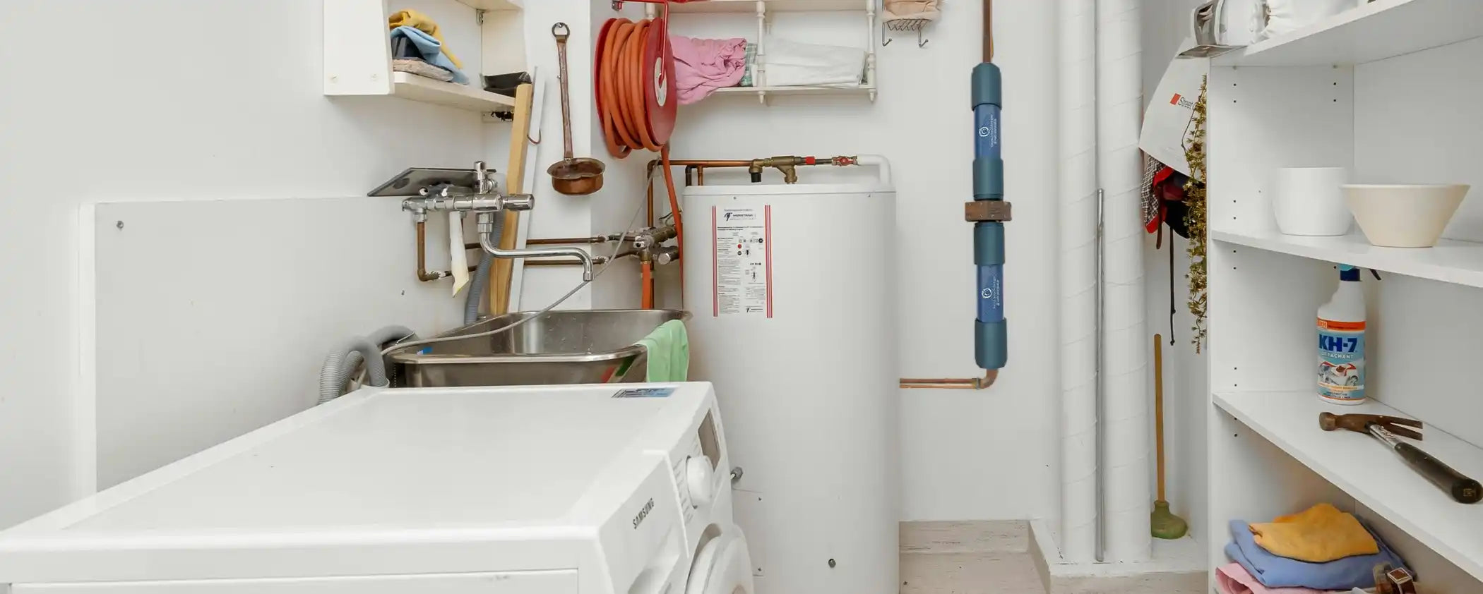 Small utility room with washing machine, dryer, shelves, and Natural Action Whole Home MagnaRay water structuring unit.